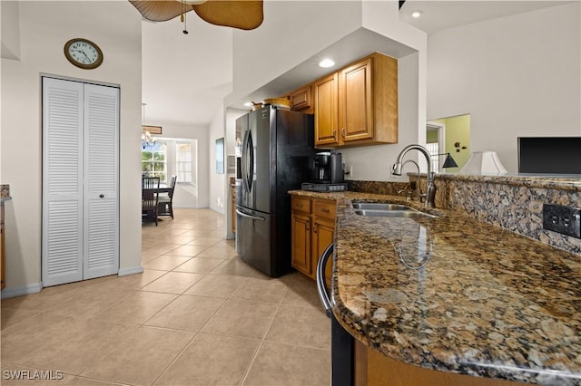 kitchen featuring kitchen peninsula, dark stone counters, ceiling fan with notable chandelier, sink, and light tile patterned floors