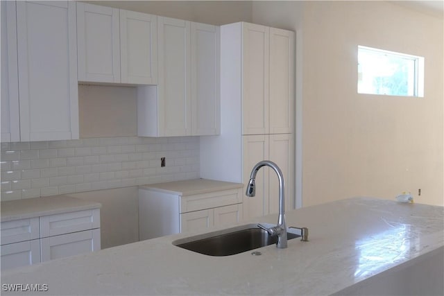 kitchen featuring backsplash, light stone countertops, sink, and white cabinets