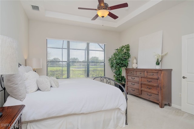 bedroom with a tray ceiling, light colored carpet, visible vents, and a ceiling fan