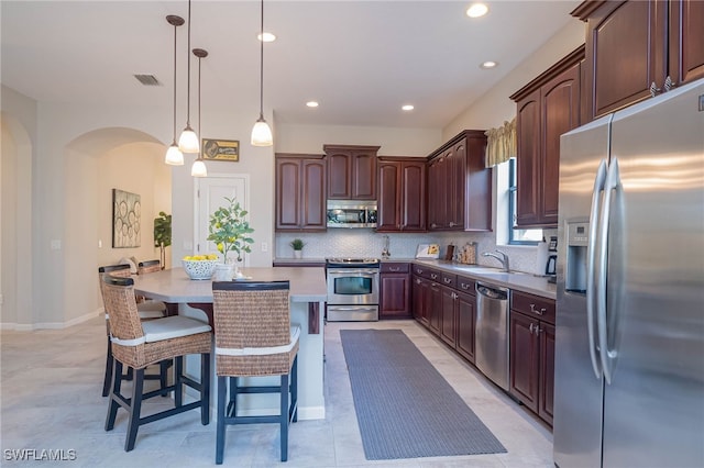 kitchen featuring arched walkways, a center island, tasteful backsplash, appliances with stainless steel finishes, and a kitchen bar