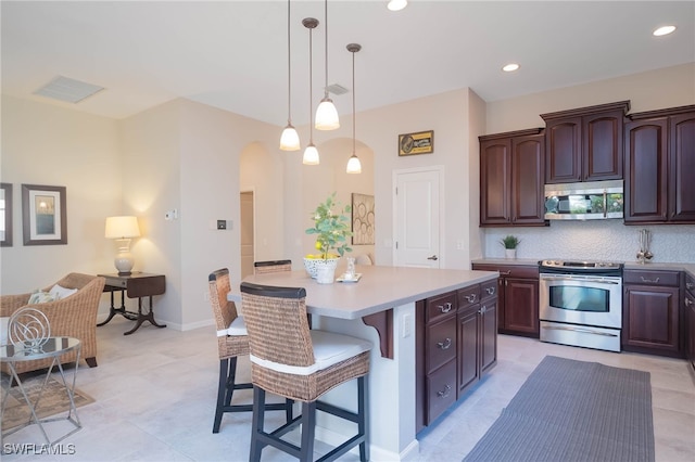 kitchen with arched walkways, decorative backsplash, light countertops, appliances with stainless steel finishes, and a kitchen bar