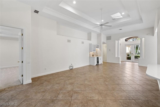 unfurnished living room featuring a tray ceiling, ceiling fan, french doors, and light tile patterned floors