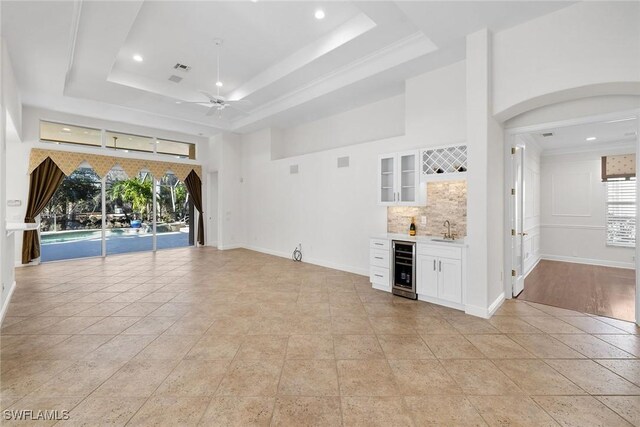 interior space featuring ceiling fan, wine cooler, indoor wet bar, a tray ceiling, and light tile patterned floors