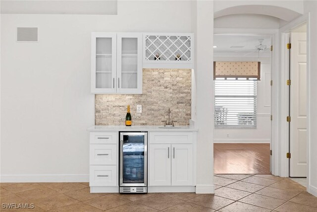 bar featuring sink, wine cooler, decorative backsplash, light tile patterned flooring, and white cabinetry