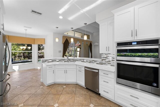 kitchen featuring kitchen peninsula, backsplash, stainless steel appliances, pendant lighting, and white cabinetry