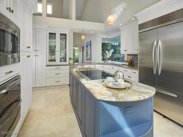 kitchen with white cabinetry, light stone counters, high vaulted ceiling, built in appliances, and a kitchen island