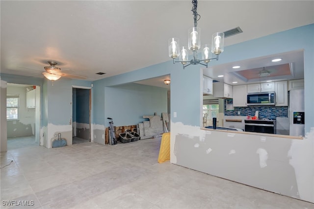 kitchen with hanging light fixtures, stainless steel appliances, a tray ceiling, white cabinets, and ceiling fan with notable chandelier