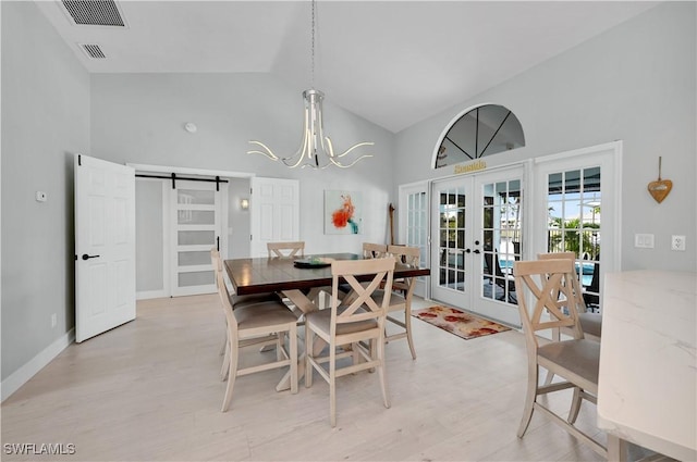 dining room featuring a barn door, a notable chandelier, light hardwood / wood-style floors, high vaulted ceiling, and french doors