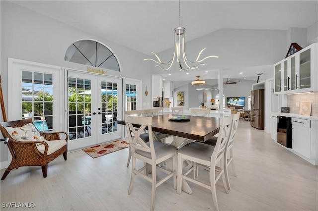 dining room featuring beverage cooler, french doors, high vaulted ceiling, ceiling fan with notable chandelier, and light hardwood / wood-style flooring