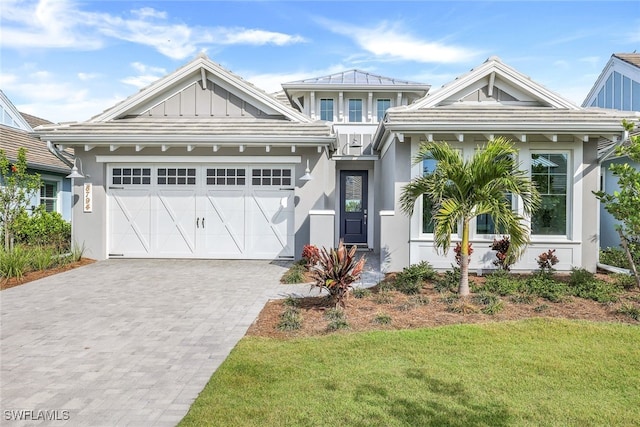 view of front of home with decorative driveway, stucco siding, board and batten siding, a front yard, and a garage