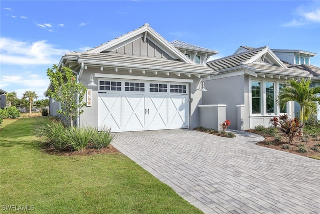 view of front of house with decorative driveway, stucco siding, board and batten siding, a garage, and a front lawn