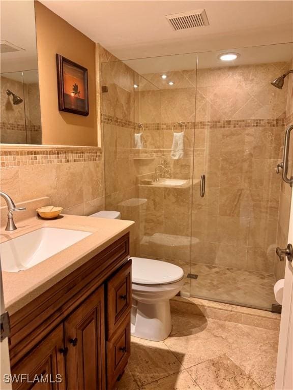 bathroom featuring vanity, toilet, a shower with shower door, and tile walls