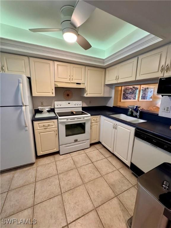 kitchen with sink, light tile patterned floors, ceiling fan, a raised ceiling, and white appliances