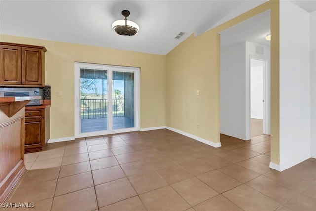 unfurnished dining area with light tile patterned floors and vaulted ceiling