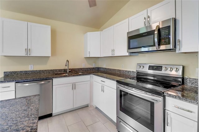 kitchen with lofted ceiling, dark stone counters, white cabinets, sink, and appliances with stainless steel finishes