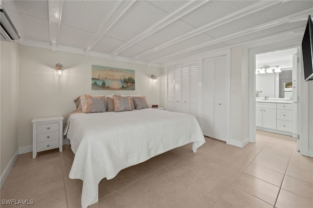 bedroom featuring light tile patterned flooring, a wall unit AC, and ensuite bath