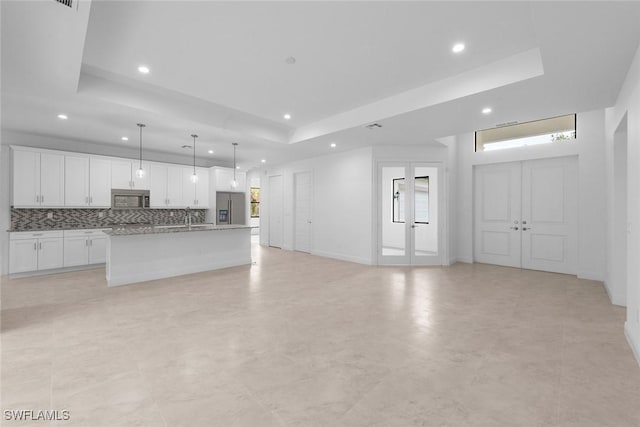 kitchen featuring a raised ceiling, white cabinetry, an island with sink, and appliances with stainless steel finishes