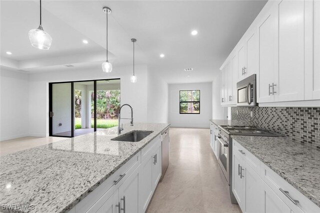 kitchen with light stone counters, stainless steel appliances, sink, white cabinetry, and hanging light fixtures