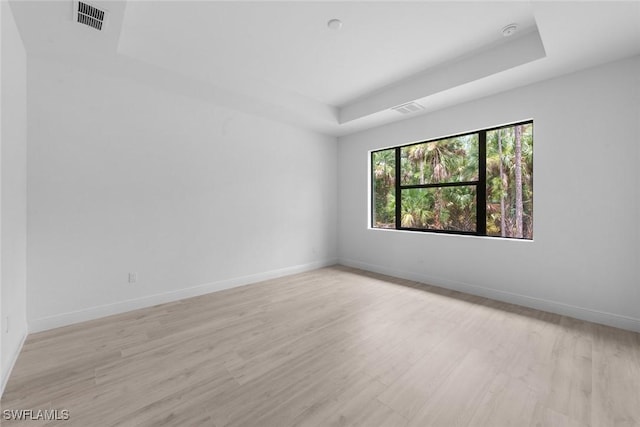 unfurnished room featuring a tray ceiling and light hardwood / wood-style floors