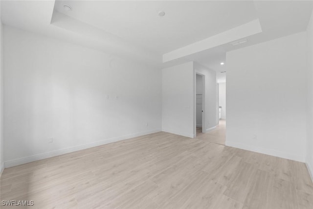 spare room with light hardwood / wood-style flooring and a raised ceiling