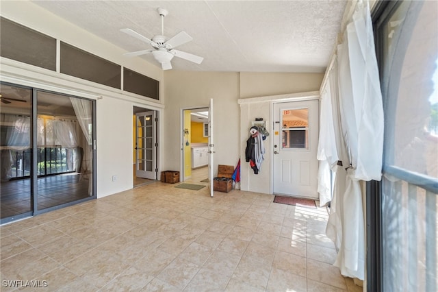 interior space with a textured ceiling, vaulted ceiling, ceiling fan, and light tile patterned flooring