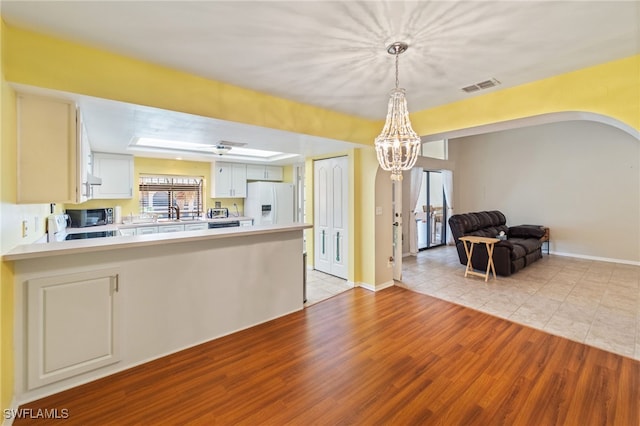 kitchen with pendant lighting, white refrigerator with ice dispenser, white cabinets, light hardwood / wood-style flooring, and kitchen peninsula