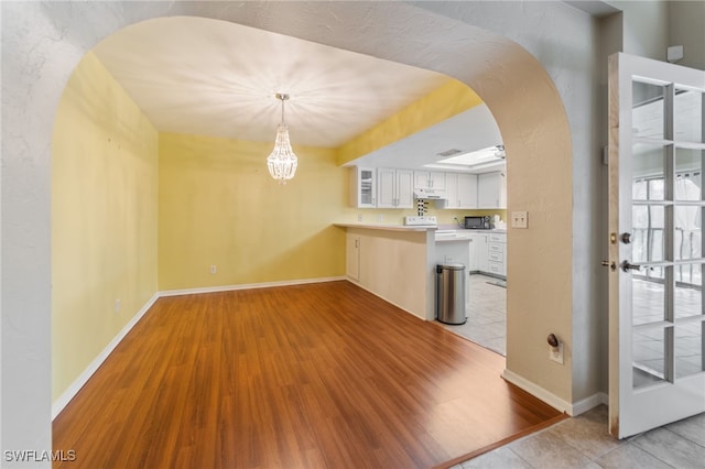 kitchen featuring white cabinets, decorative light fixtures, kitchen peninsula, and light hardwood / wood-style flooring