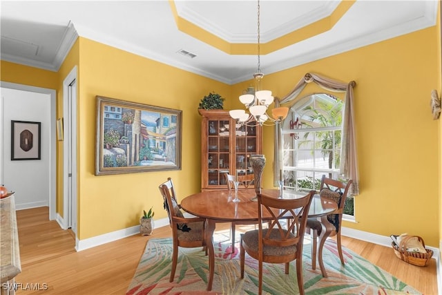 dining area featuring a chandelier, light hardwood / wood-style flooring, crown molding, and a tray ceiling