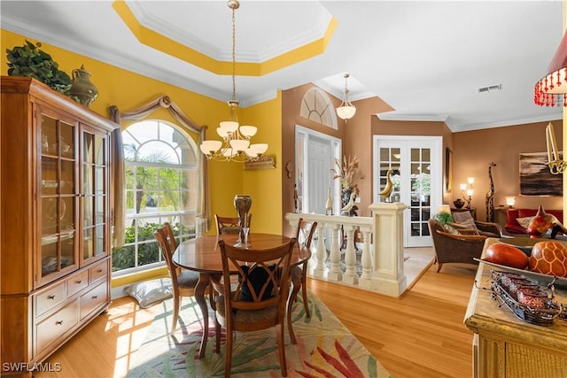 dining room featuring french doors, light wood-type flooring, ornamental molding, a raised ceiling, and an inviting chandelier