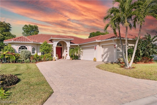 mediterranean / spanish-style home with a garage, a tiled roof, decorative driveway, a lawn, and stucco siding