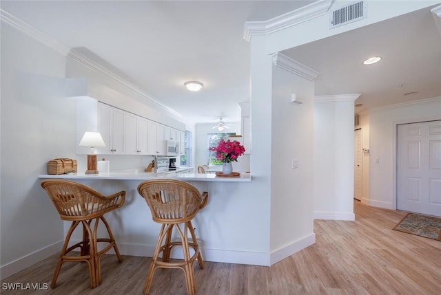 kitchen featuring a kitchen breakfast bar, kitchen peninsula, crown molding, stove, and white cabinets