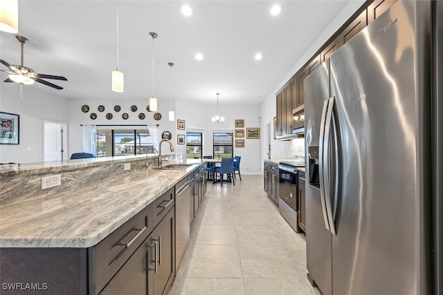 kitchen with light stone countertops, sink, stainless steel appliances, a large island with sink, and decorative light fixtures