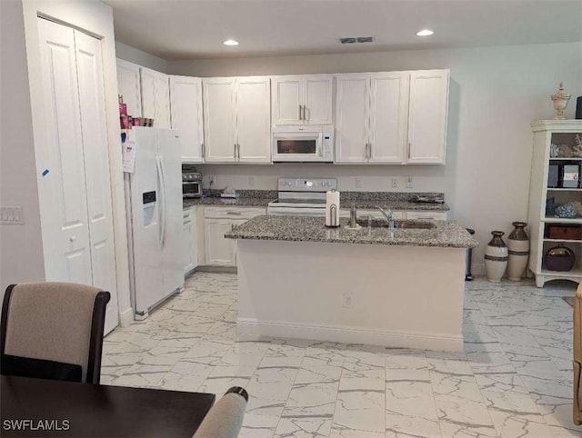 kitchen featuring white appliances, sink, stone countertops, white cabinets, and an island with sink