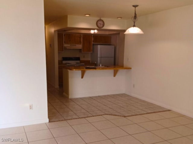 kitchen featuring a breakfast bar, kitchen peninsula, white fridge, pendant lighting, and stove