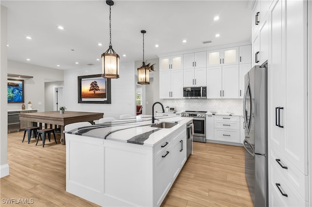 kitchen featuring light stone counters, decorative light fixtures, a center island with sink, white cabinets, and appliances with stainless steel finishes