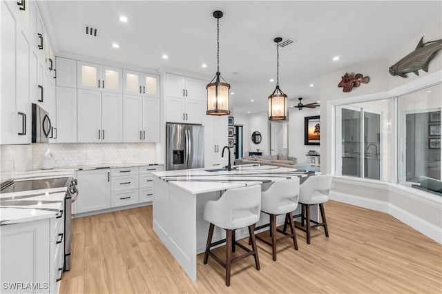 kitchen with white cabinets, ceiling fan, stainless steel appliances, and a kitchen island with sink