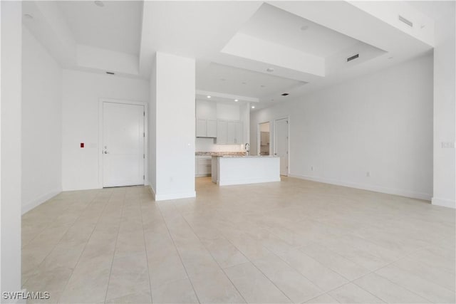 unfurnished living room with light tile patterned floors and a tray ceiling