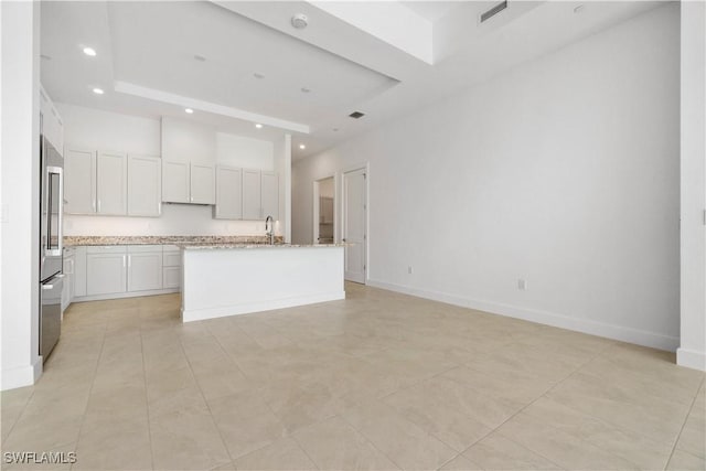 kitchen featuring white cabinets, an island with sink, sink, light stone counters, and a tray ceiling