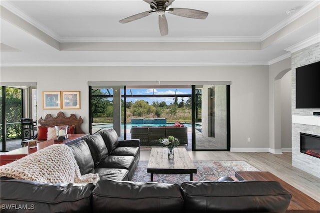 living room with light hardwood / wood-style floors, a stone fireplace, ceiling fan, and a tray ceiling