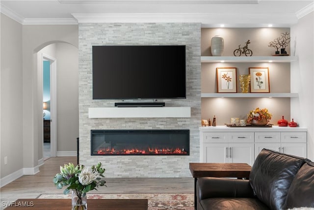 living room featuring a stone fireplace, built in features, ornamental molding, and light hardwood / wood-style flooring