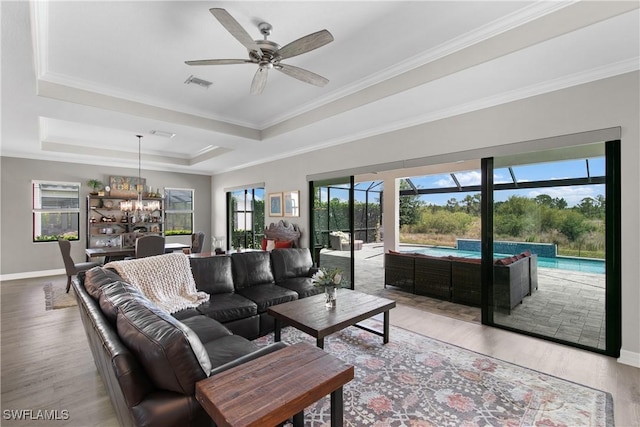 living room featuring a raised ceiling, crown molding, ceiling fan with notable chandelier, and hardwood / wood-style flooring