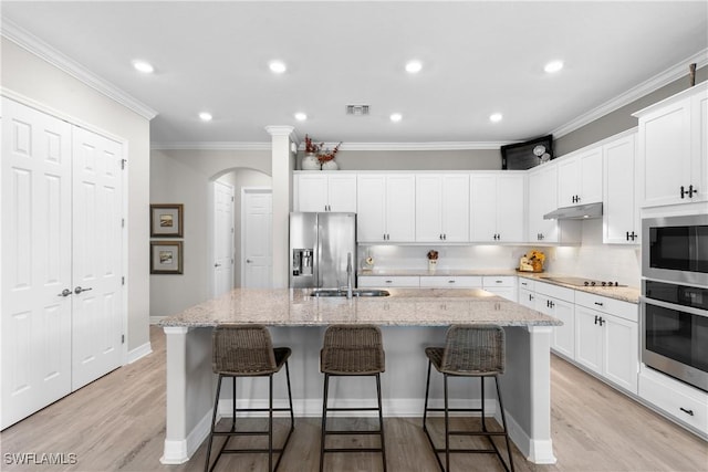 kitchen with light hardwood / wood-style floors, light stone countertops, a kitchen island with sink, and appliances with stainless steel finishes