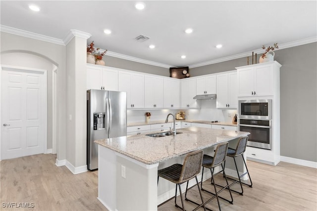 kitchen with appliances with stainless steel finishes, light stone counters, a kitchen island with sink, sink, and white cabinetry