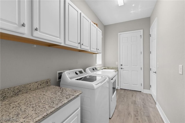 clothes washing area with washer and clothes dryer, cabinets, and light hardwood / wood-style floors