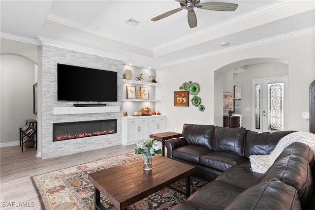 living room with ceiling fan, a fireplace, crown molding, and light wood-type flooring