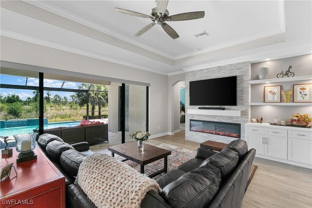 living room featuring a raised ceiling, a stone fireplace, built in features, and light hardwood / wood-style floors