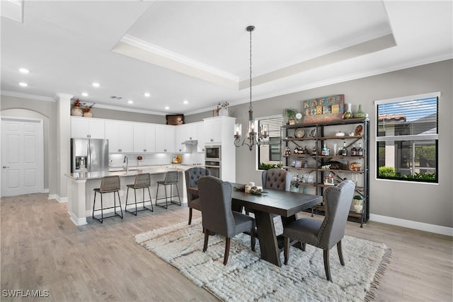 dining space featuring a tray ceiling, crown molding, sink, and light hardwood / wood-style flooring