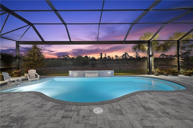 pool at dusk with pool water feature, a patio area, and a lanai