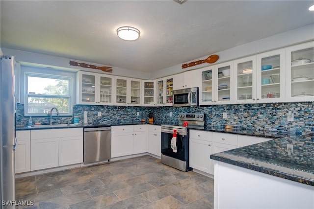 kitchen featuring white cabinetry, sink, stainless steel appliances, backsplash, and dark stone countertops