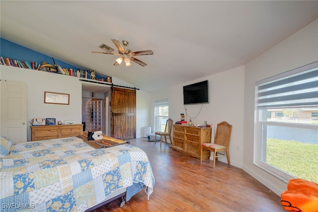 bedroom with hardwood / wood-style floors, ceiling fan, a barn door, and vaulted ceiling